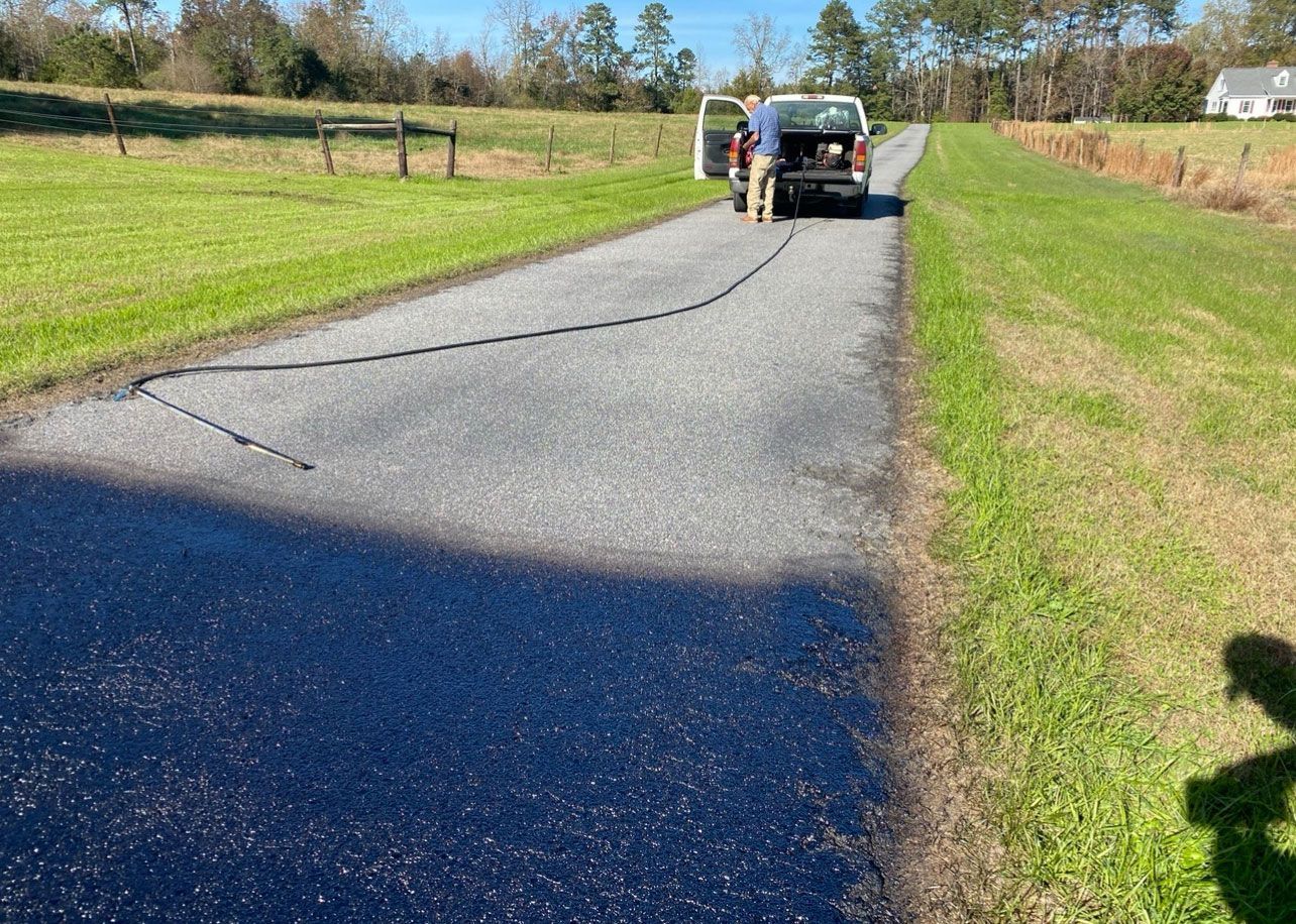 Worker by a truck on a rural road, with a long dark cable or hose stretching across the pavement