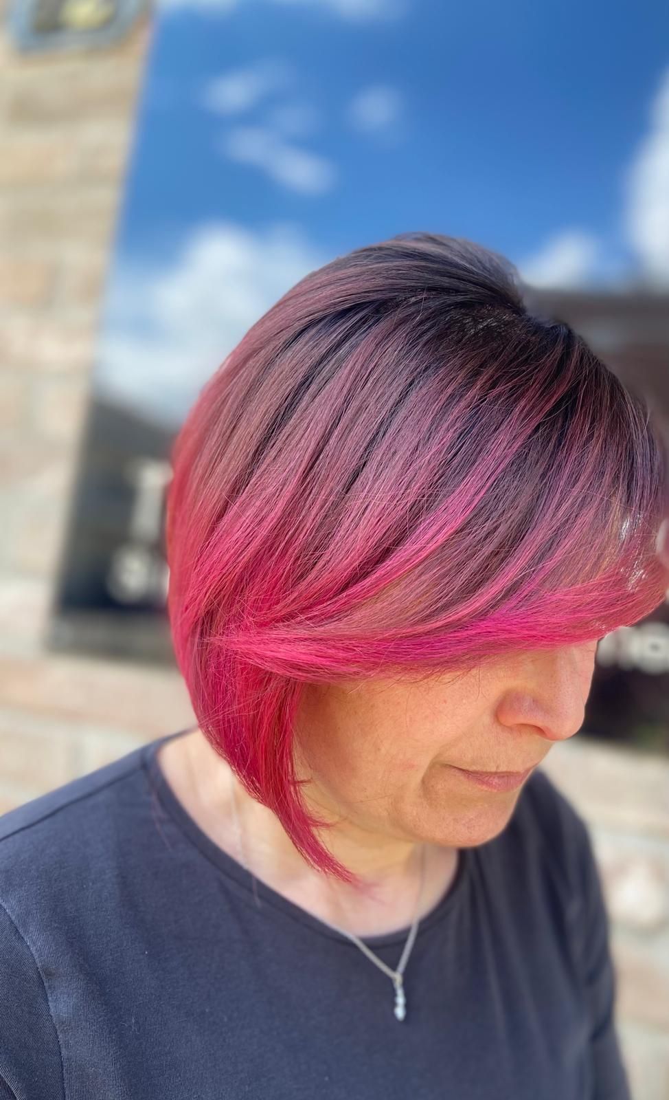 Donna con acconciatura a caschetto sfumata rosa e nera, indossa un top scuro, all'aperto.