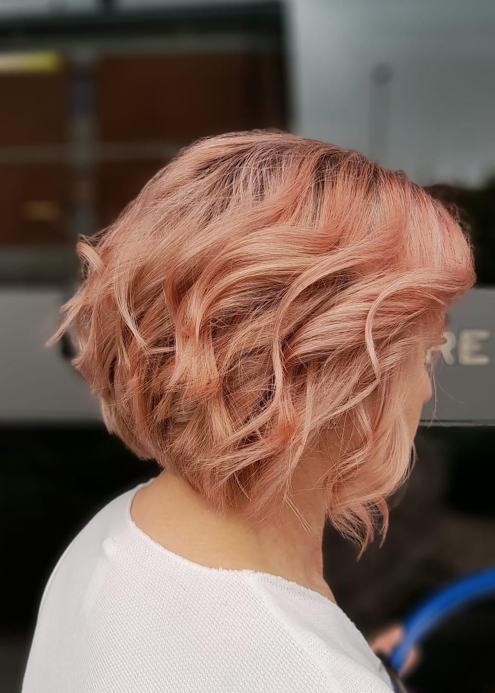 Donna con taglio di capelli biondo-rosato ondulato, che indossa un maglione bianco.
