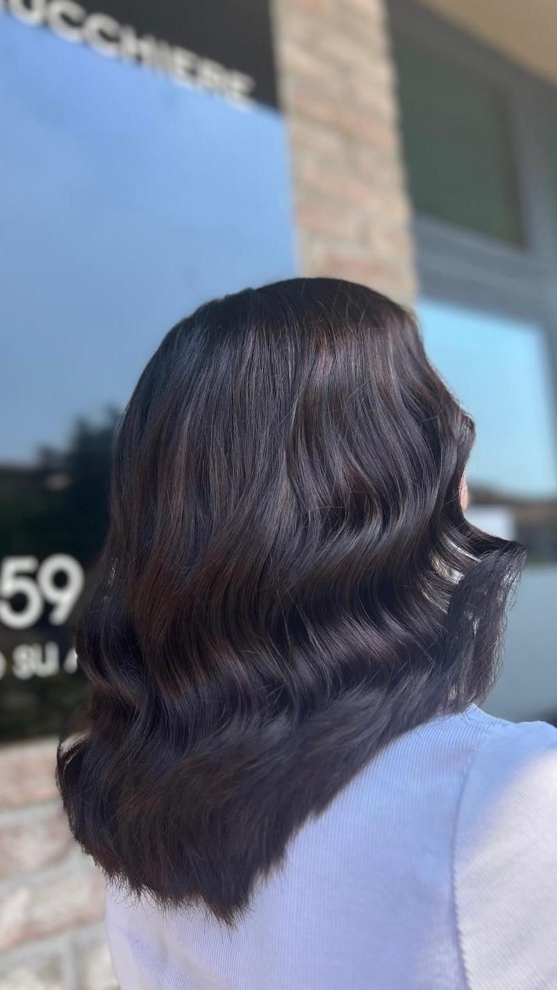 Donna con capelli scuri e ondulati, acconciati secondo lo stile vintage delle onde; fuori da un salone.