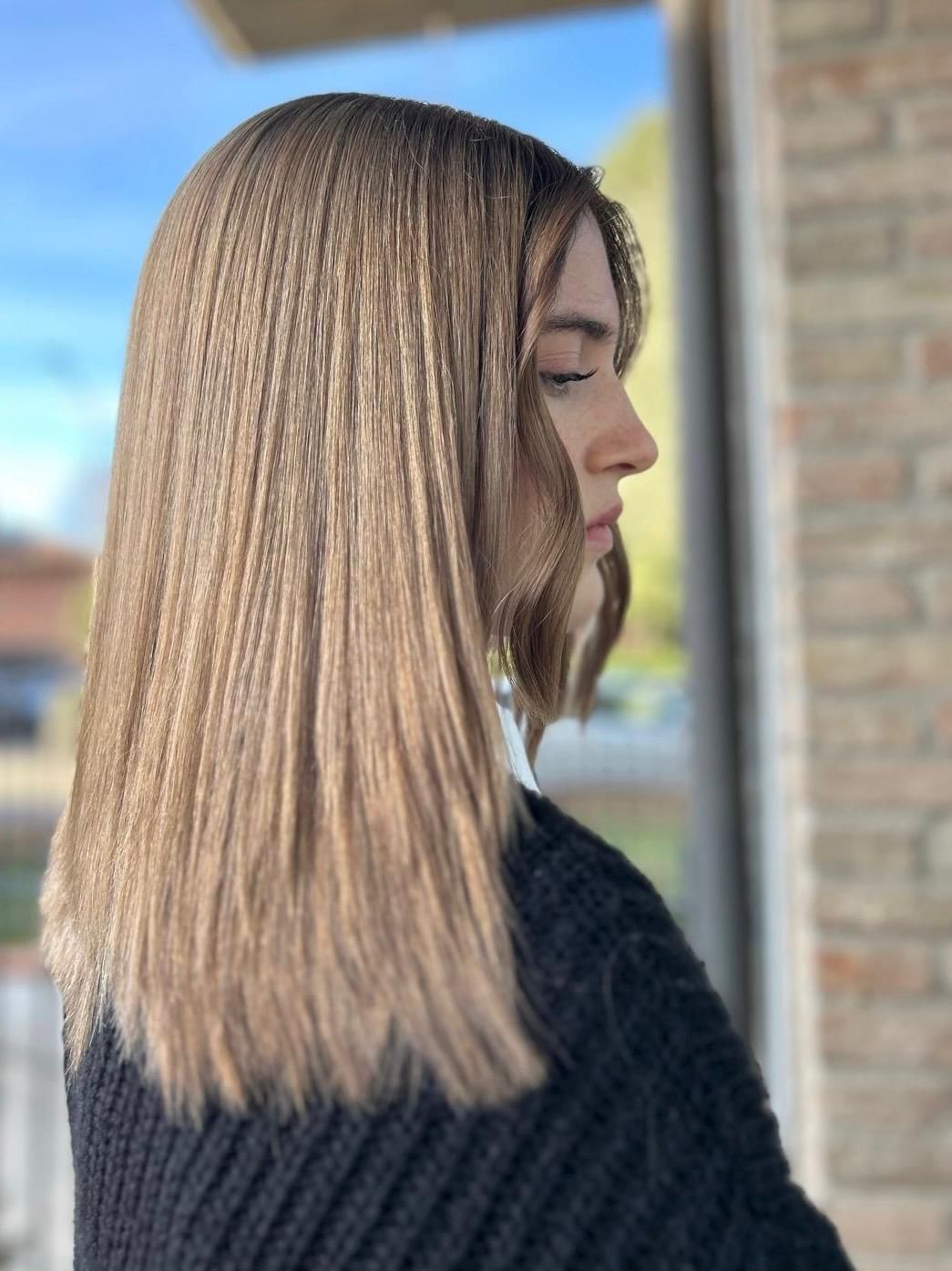 Donna con capelli castano chiaro e mossi, viso spigoloso, maglione nero. Esterno, sfondo di mattoni.