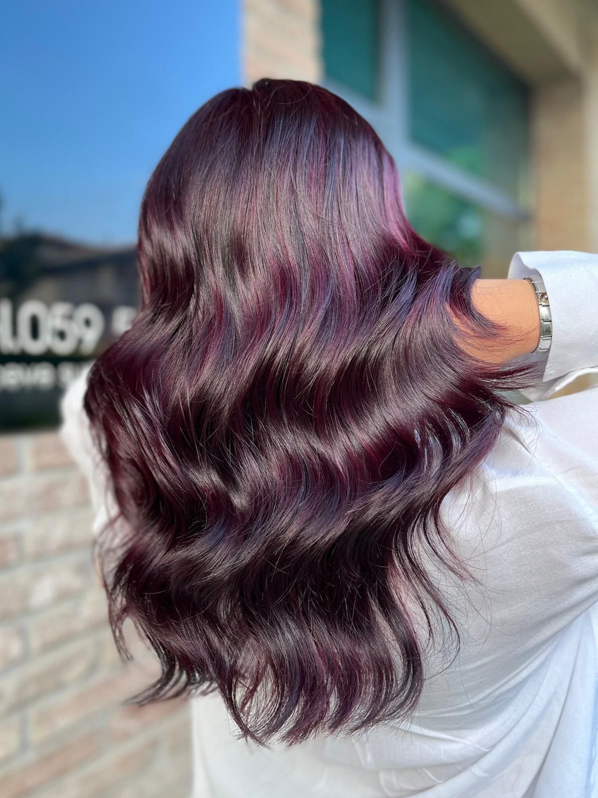 Capelli mossi, viola scuro; una persona è girata di spalle e indossa una camicia bianca; all'aperto, sfondo sfocato.