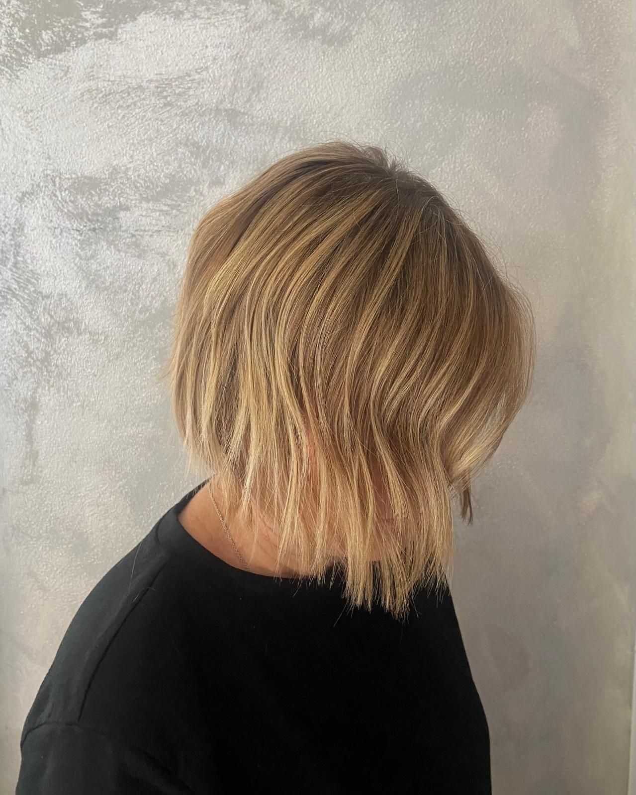 Donna con un caschetto biondo strutturato contro una parete argentata.