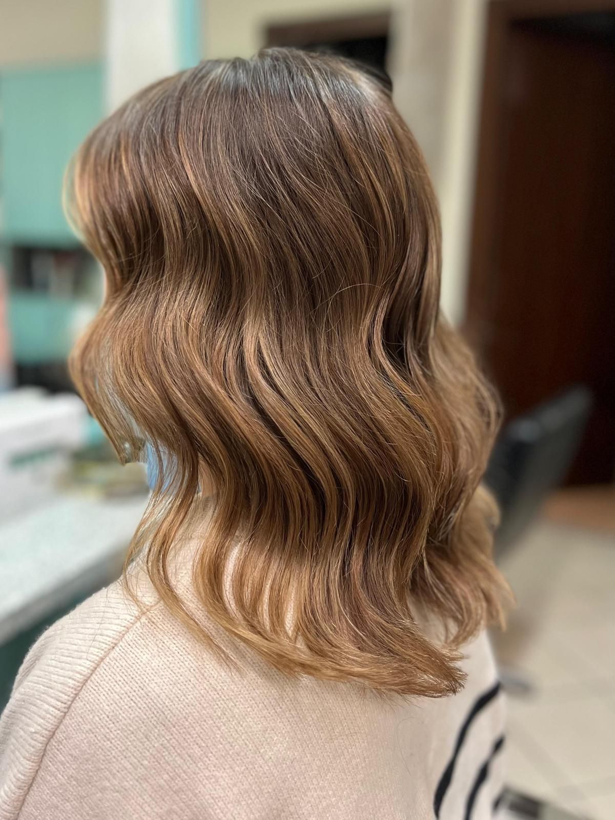 Capelli castani ondulati lunghi fino alle spalle, acconciati in un salone di bellezza, con riflessi più chiari.