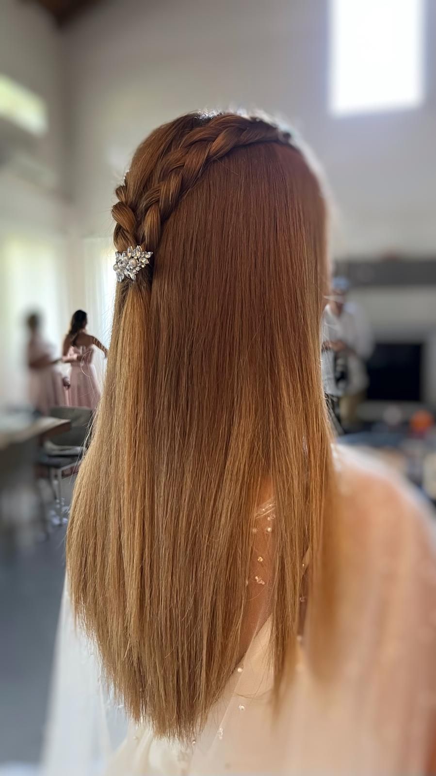 Donna con lunghi capelli castani ondulati, una corona intrecciata e un fermaglio per capelli decorato con gioielli. All'interno, sfondo sfocato.