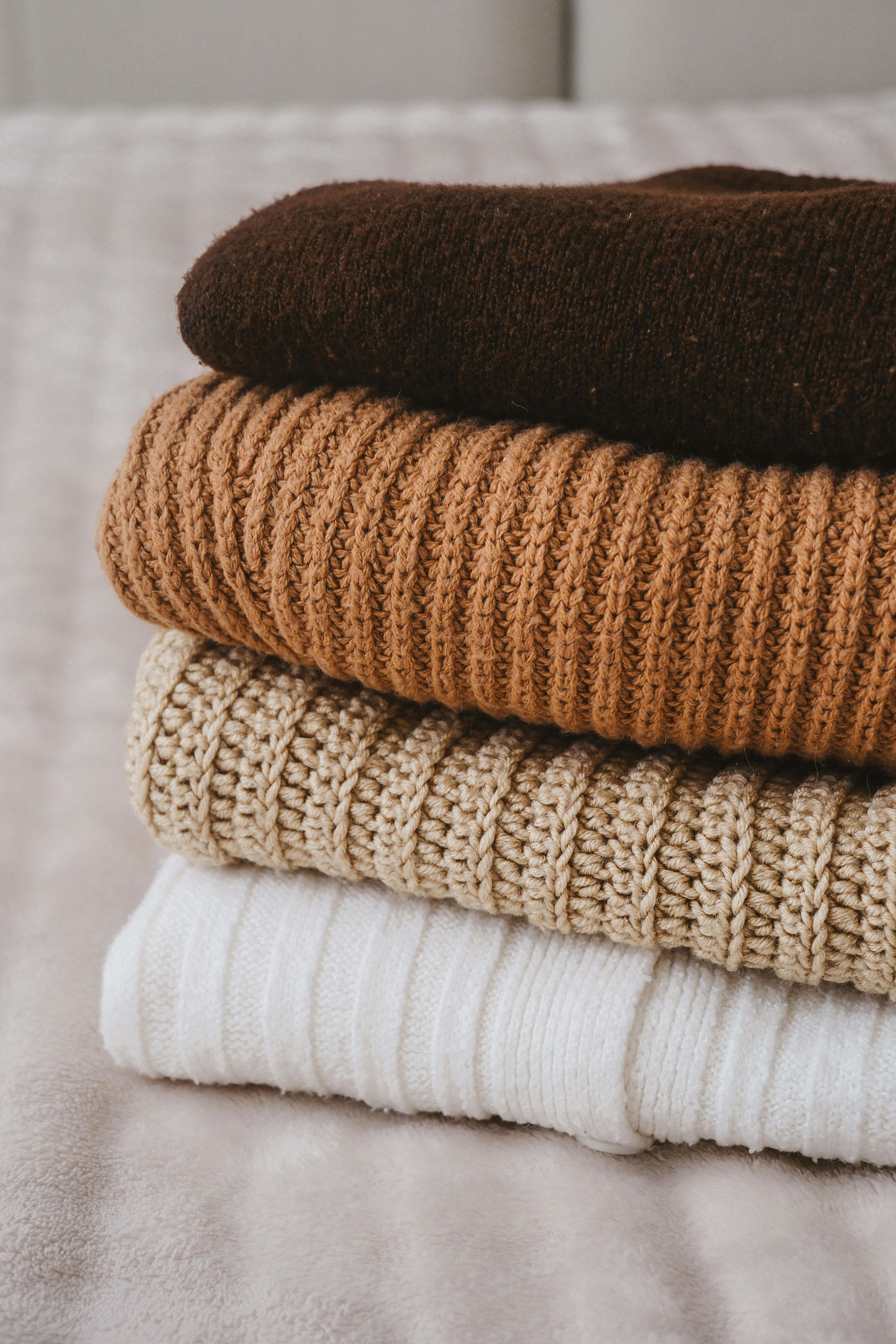 A pile of sweaters stacked on top of each other on a bed.