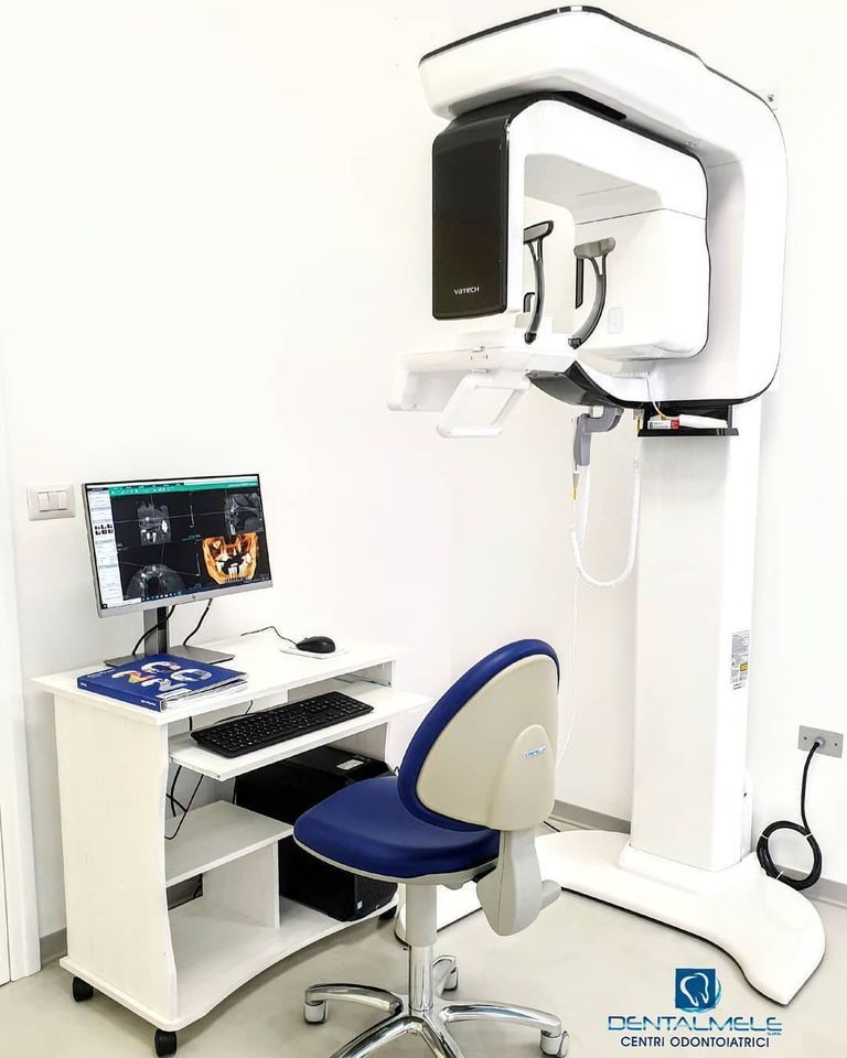 Studio dentistico con scanner radiografico 3D bianco, monitor del computer e poltrona blu.