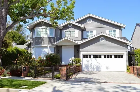 Gray two-story house with white trim, garage, and front yard with greenery and a gated entrance.