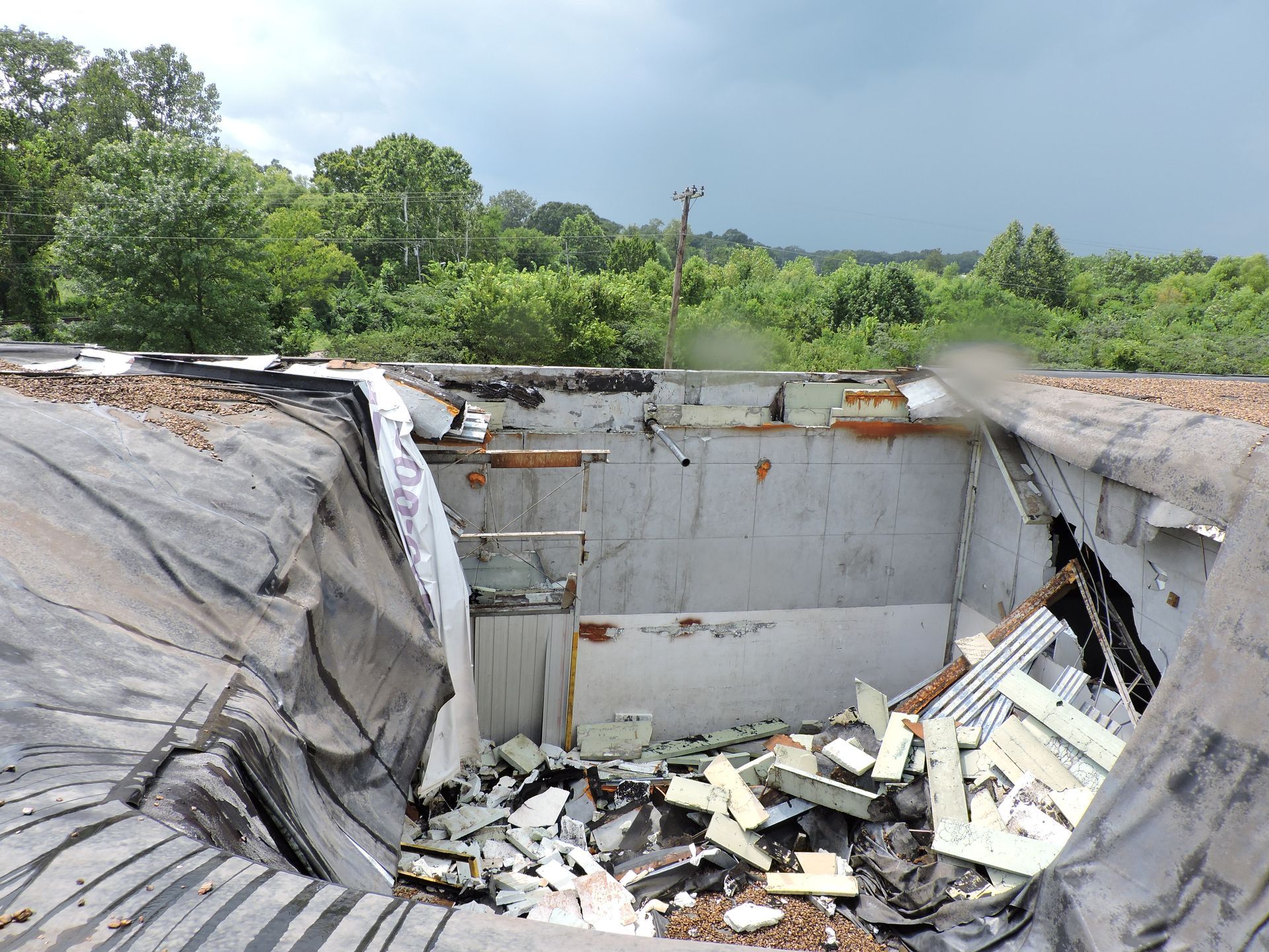 A large hole in the roof of a building with trees in the background.