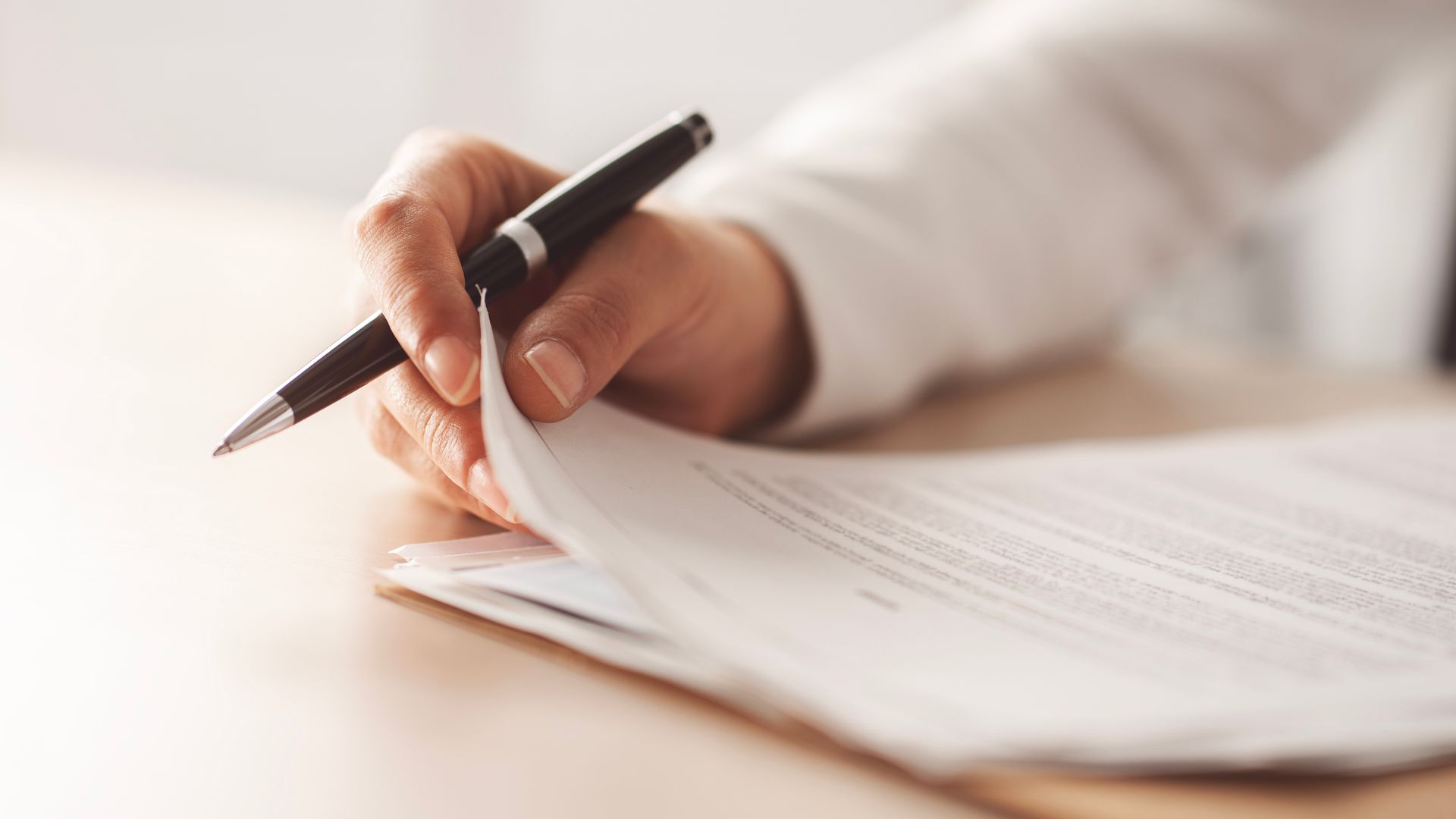 Person's hand with a pen writing on a stack of white papers, possibly signing a document. Person's hand with a pen writing on a stack of white papers, possibly signing a document.