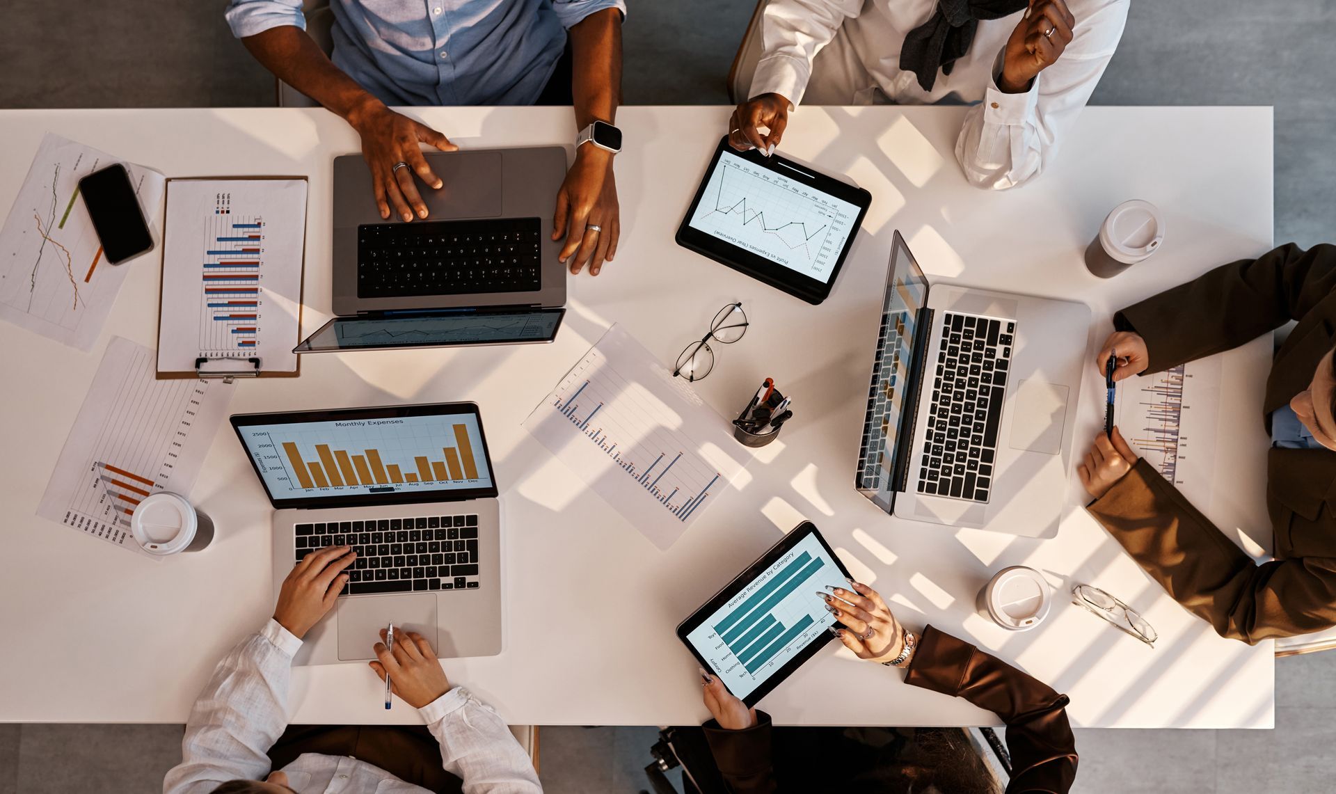 People at a table, using laptops and tablets, reviewing charts and graphs. People at a table, using laptops and tablets, reviewing charts and graphs.
