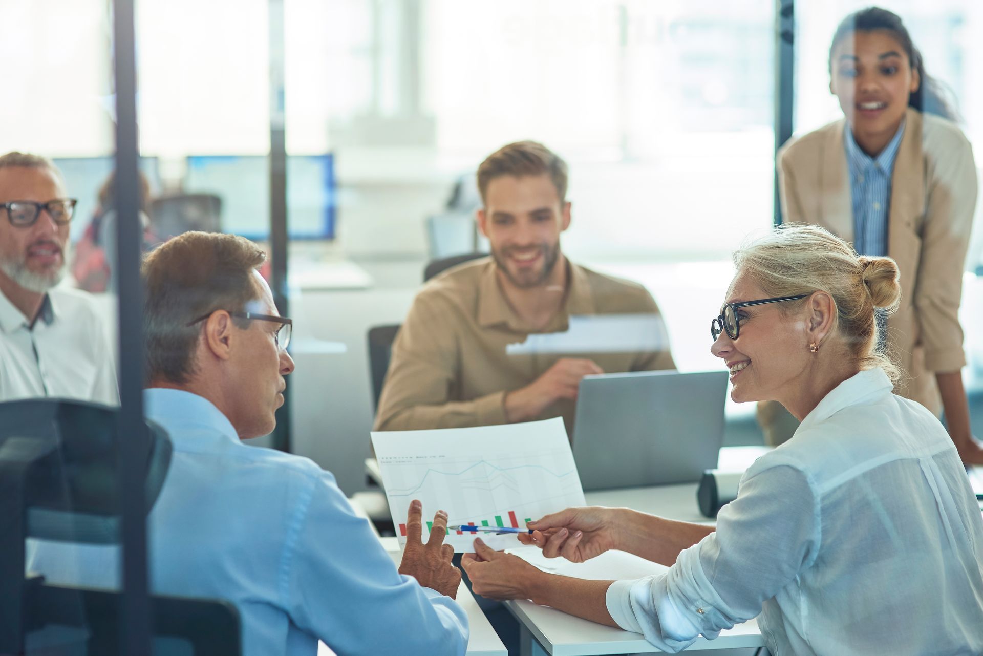 People in a meeting room, looking at documents and a laptop, discussing. People in a meeting room, looking at documents and a laptop, discussing.