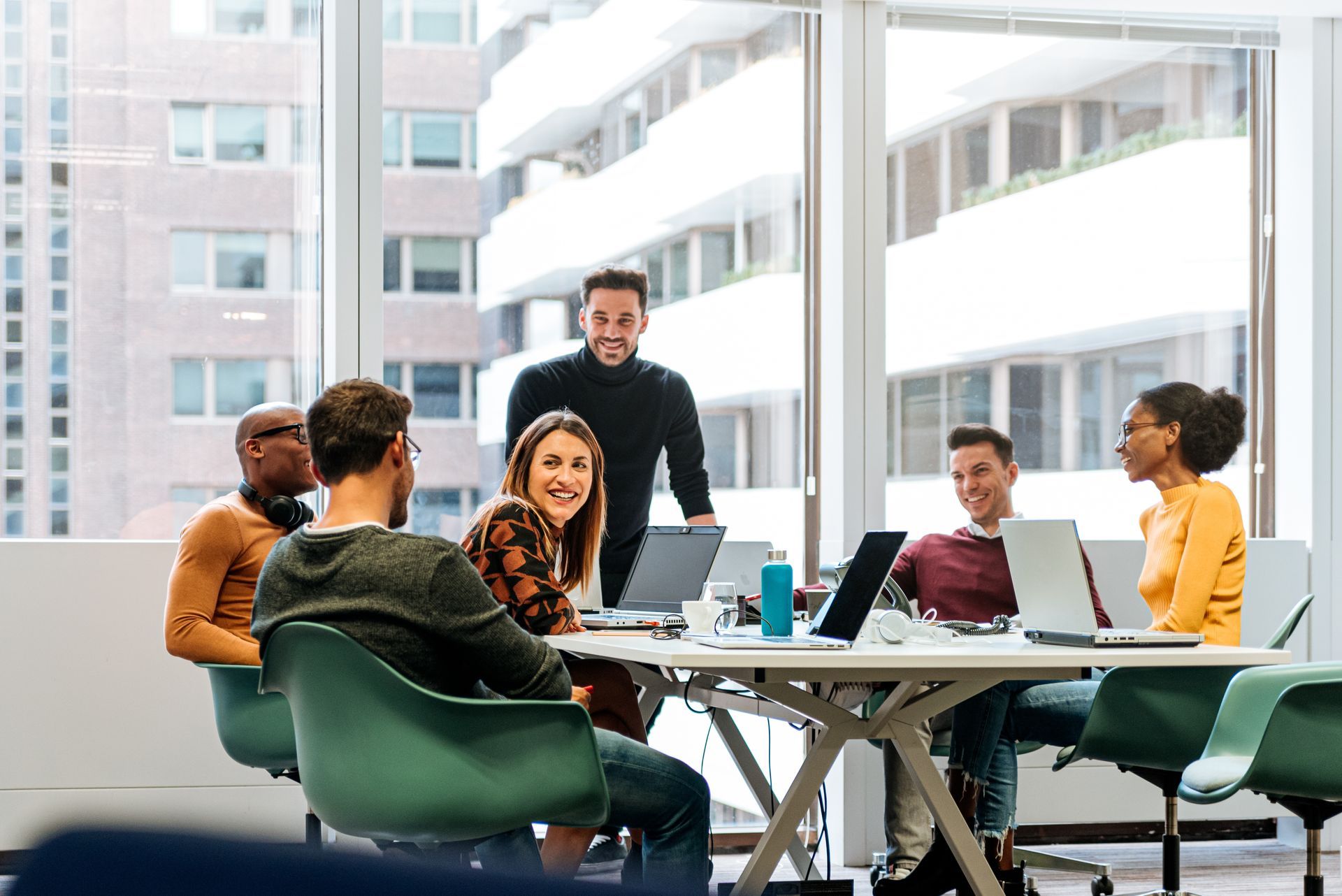 A team of people in an office meeting at a table with laptops, smiling and engaged. A team of people in an office meeting at a table with laptops, smiling and engaged.