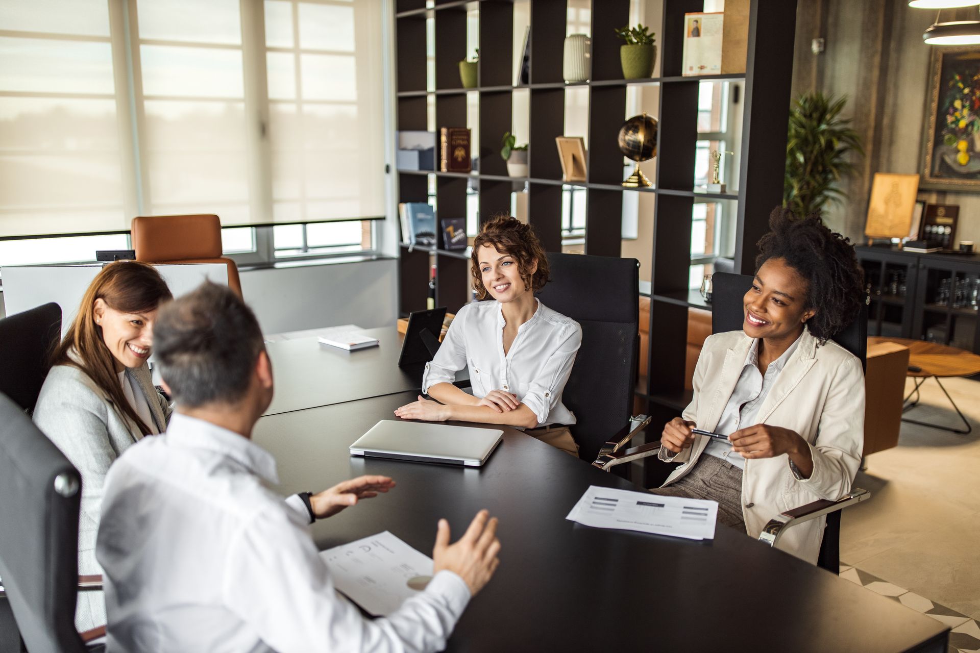 People in business attire seated around a table in a modern office, engaged in a discussion. People in business attire seated around a table in a modern office, engaged in a discussion.