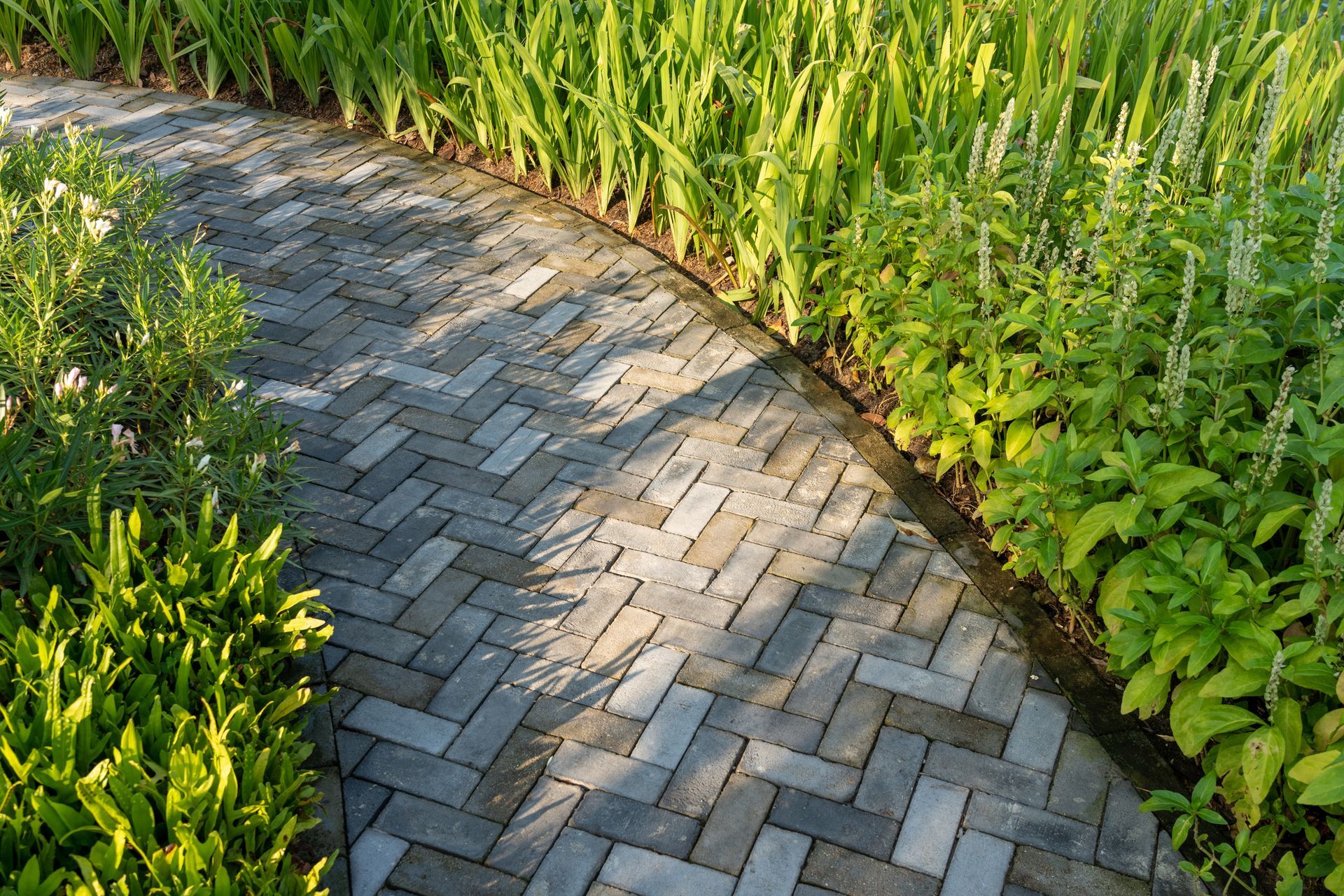A Brick Walkway in A Garden Surrounded by Grass and Bushes - Mingo, IA - Karns Concrete LLC