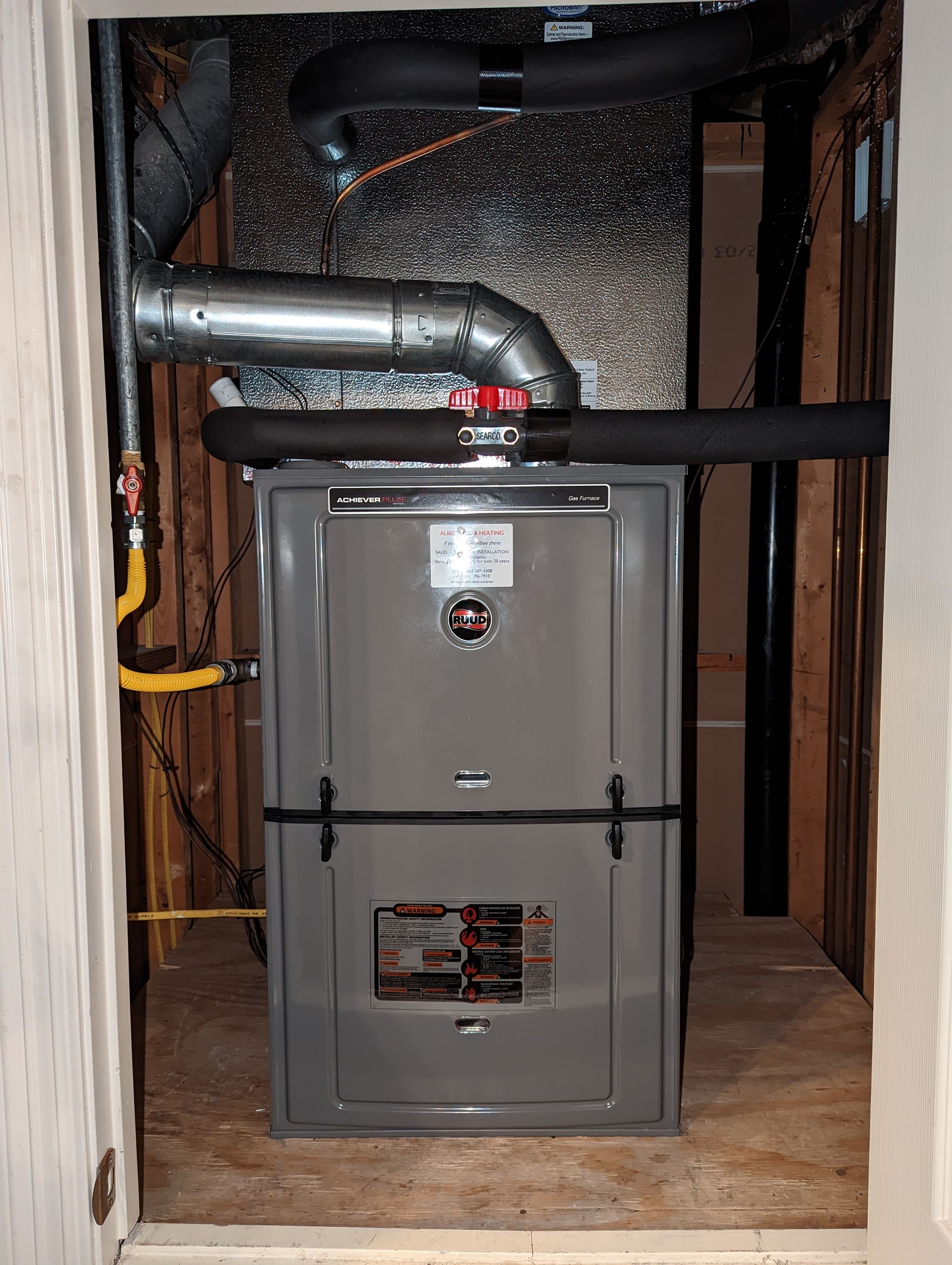 A furnace is sitting in a closet with pipes coming out of it.