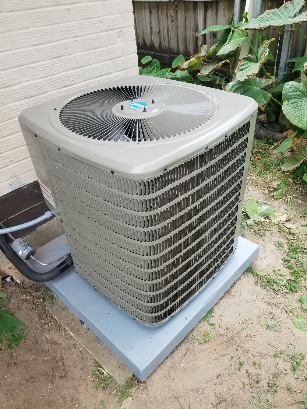 A large air conditioner is sitting outside of a brick building.