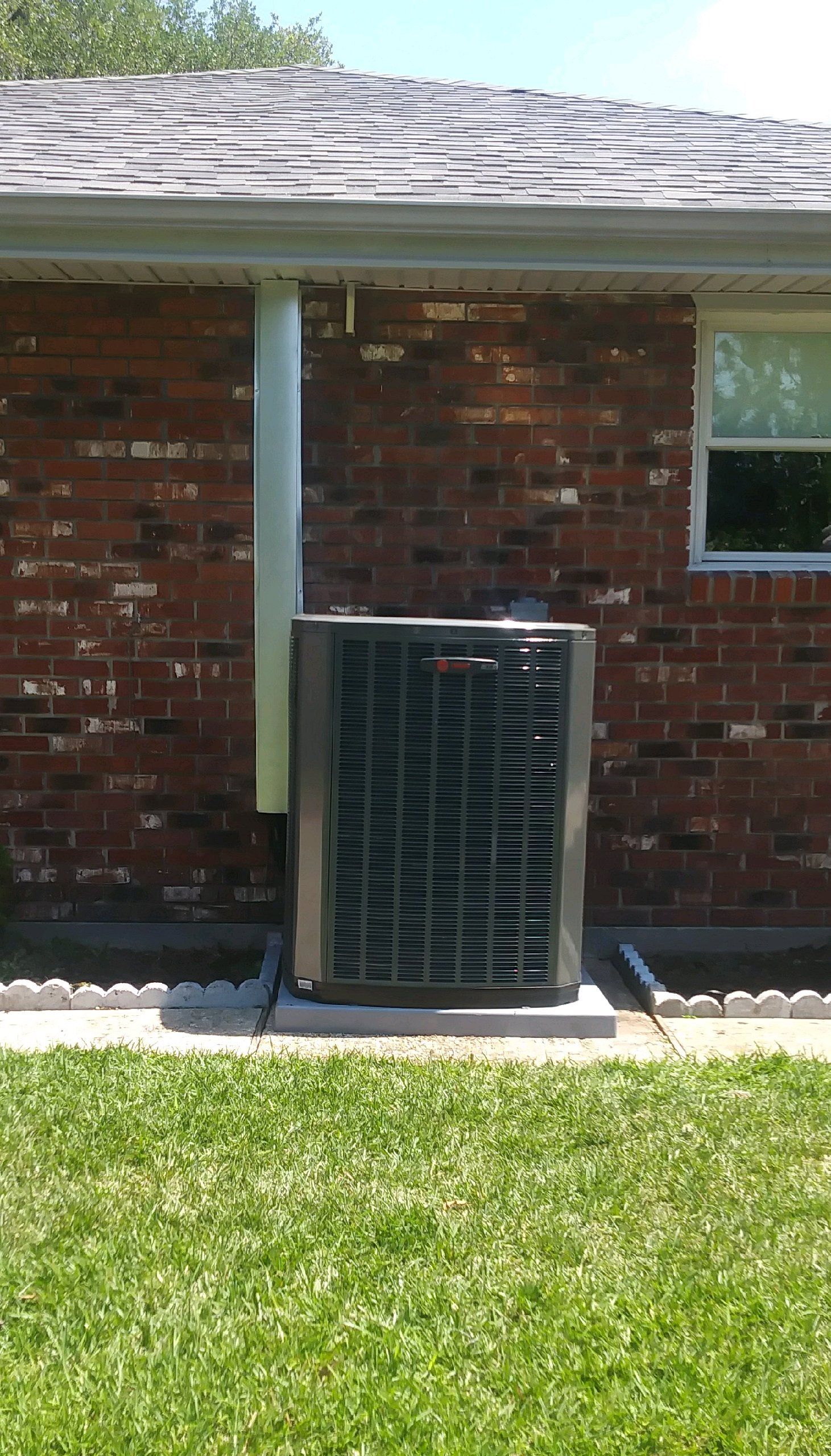 An air conditioner is sitting on the side of a brick house.