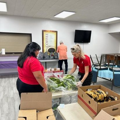 A woman in a red shirt is standing next to a table with boxes of food.