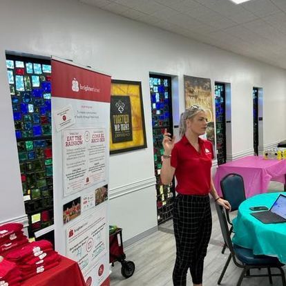 A woman in a red shirt is standing in a room with tables and chairs.