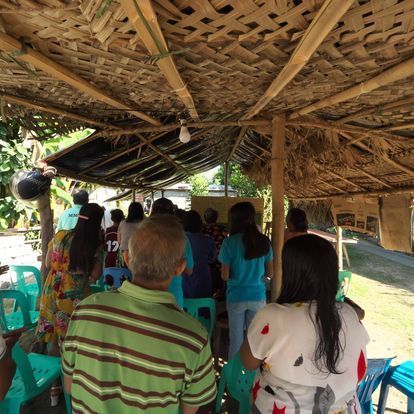 A group of people sitting under a thatched roof with one man wearing a shirt with the number 12 on it