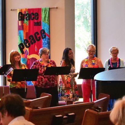 A group of women singing in front of a banner that says grace and peace