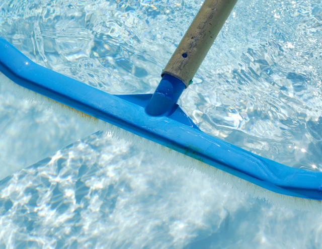 A blue broom is being used to clean a swimming pool.
