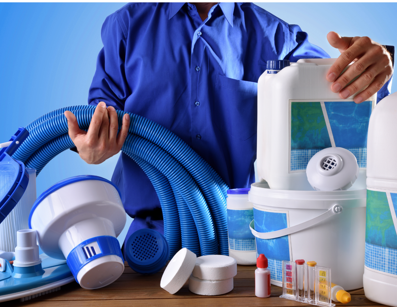 A man in a blue shirt is holding a hose surrounded by pool supplies.