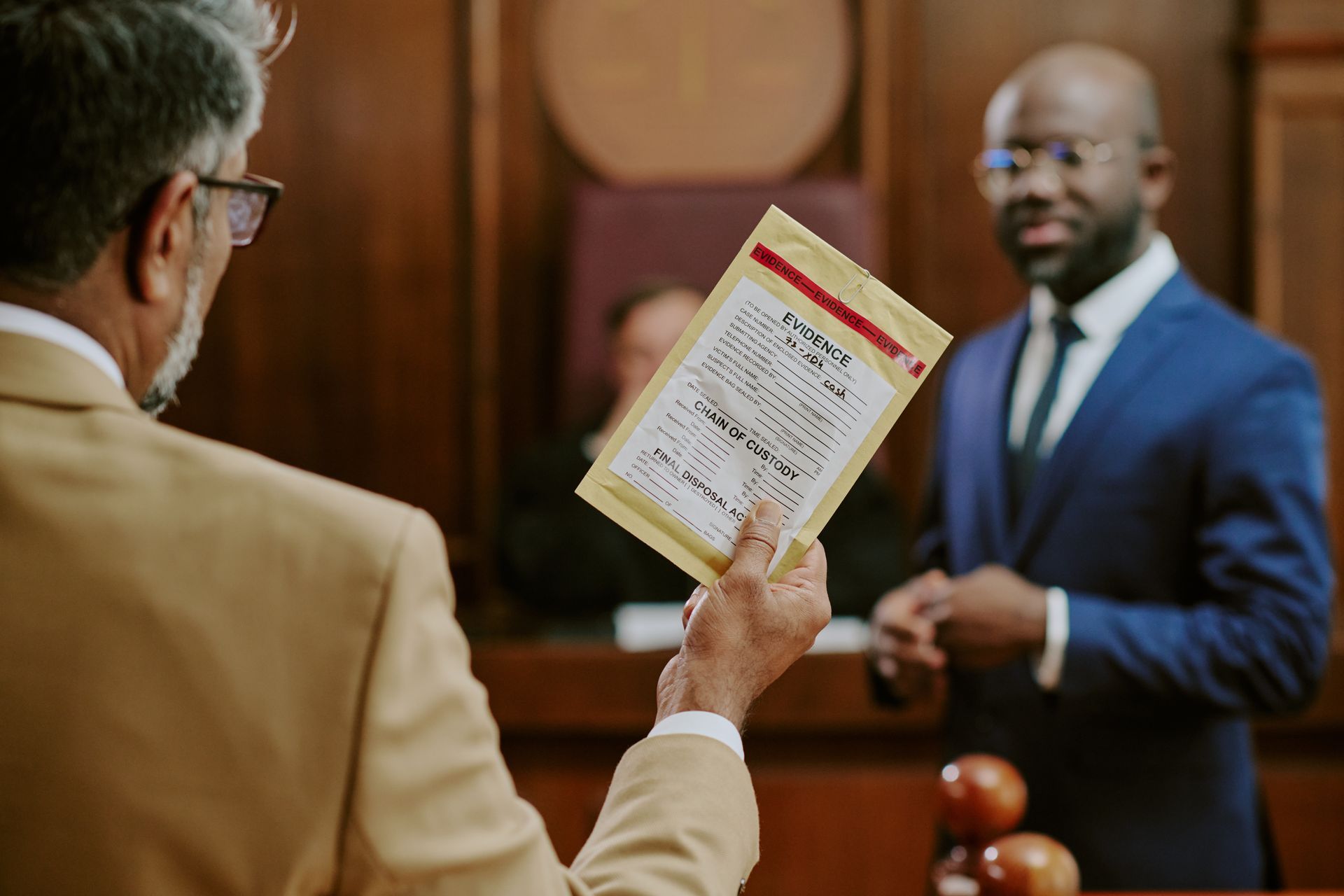 A lawyer holding an evidence bag in a courtroom with another lawyer and judge in the background.