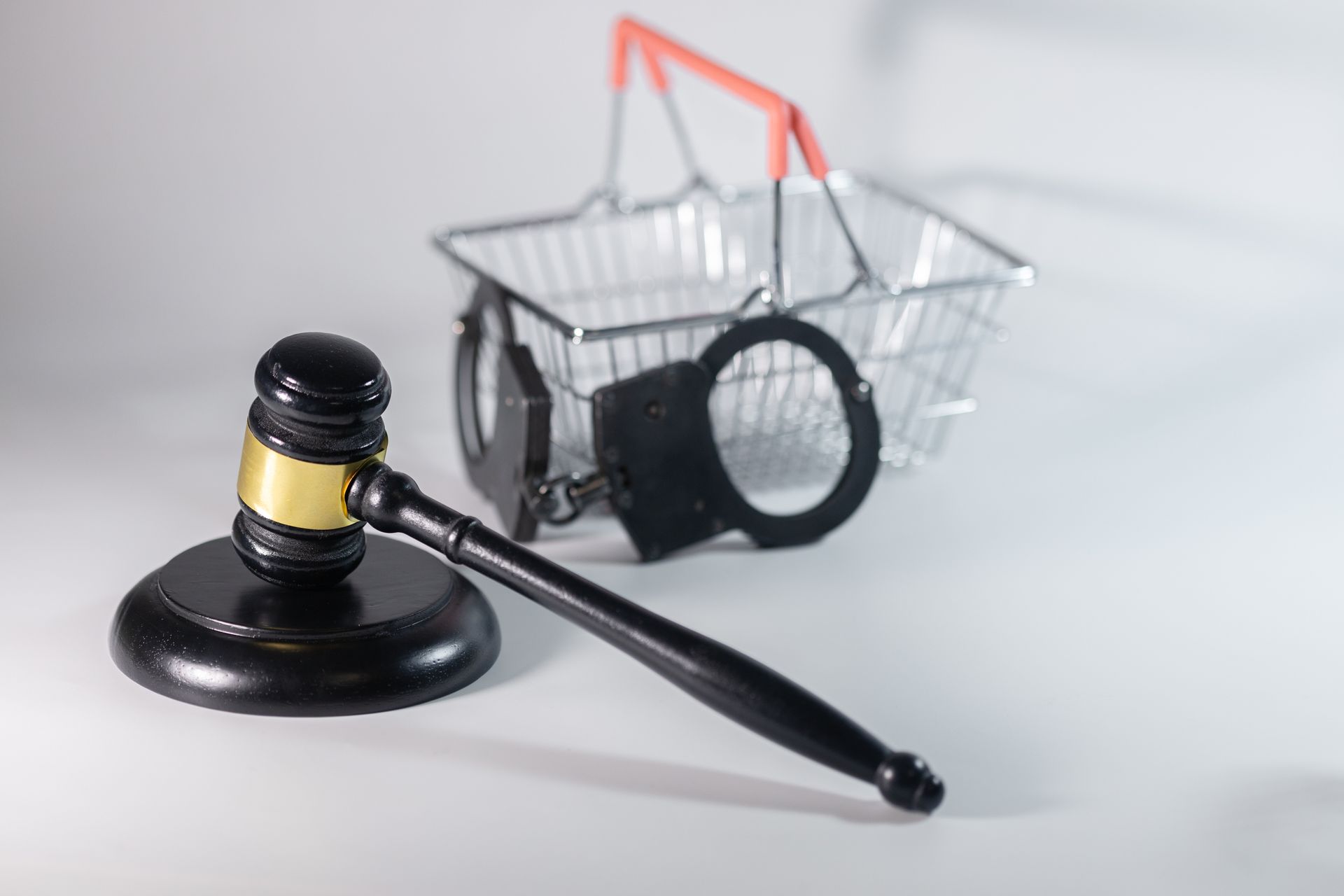 A hand holds a pair of handcuffs, next to a wooden gavel, in front of a white background.