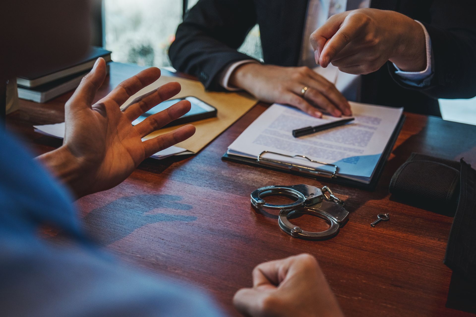 People discussing a document at a wooden table with a notebook, pen, and handcuffs nearby