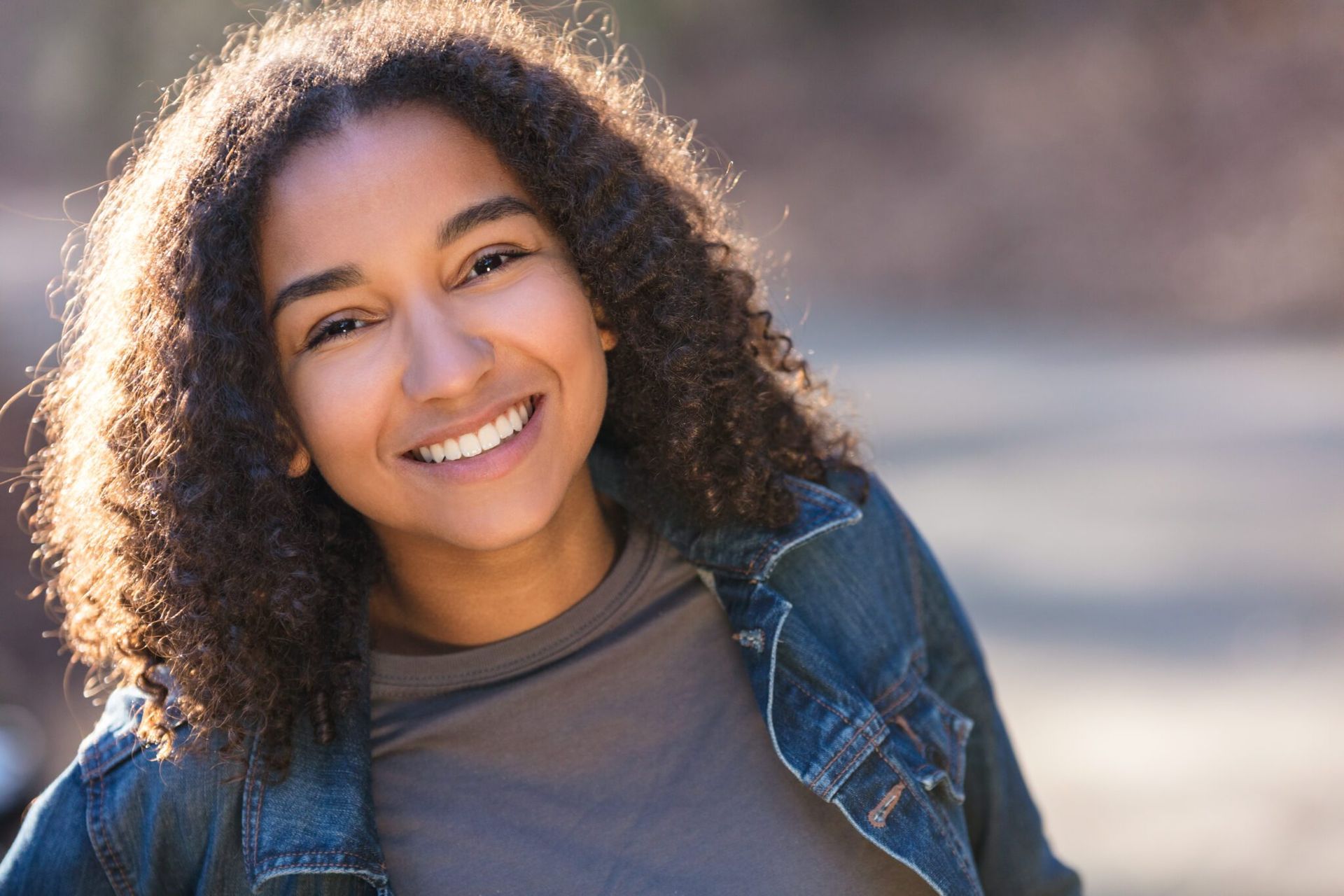 a young woman with curly hair is smiling and wearing a denim jacket .