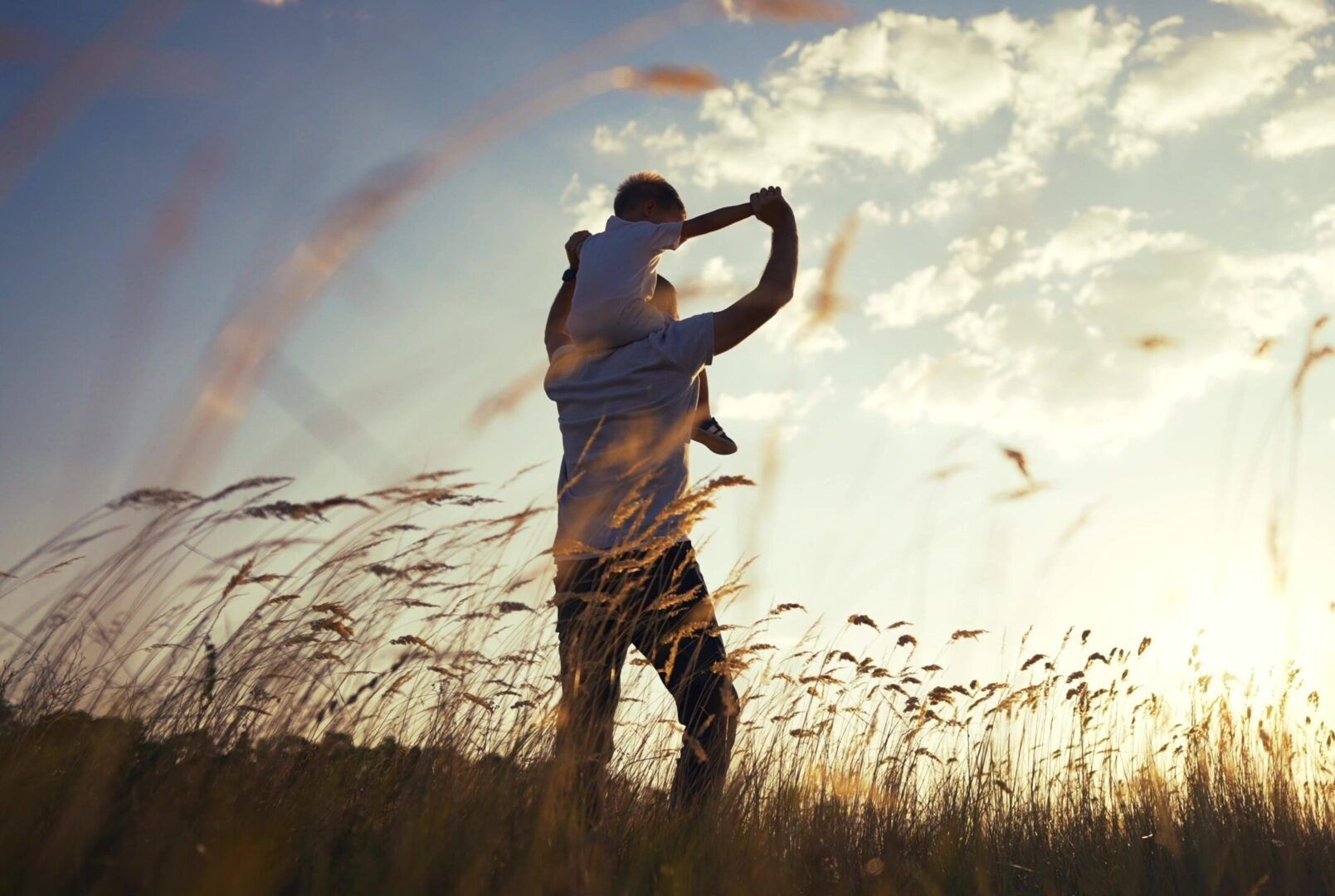 a man is carrying a baby on his shoulders in a field .
