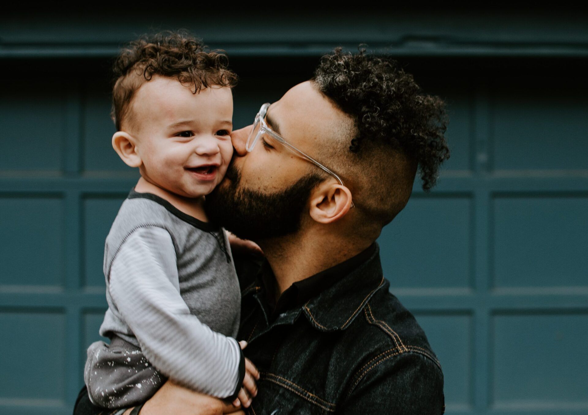 a man is holding a baby in his arms and kissing it on the cheek .