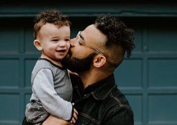 a man is holding a baby in his arms and kissing it on the cheek .