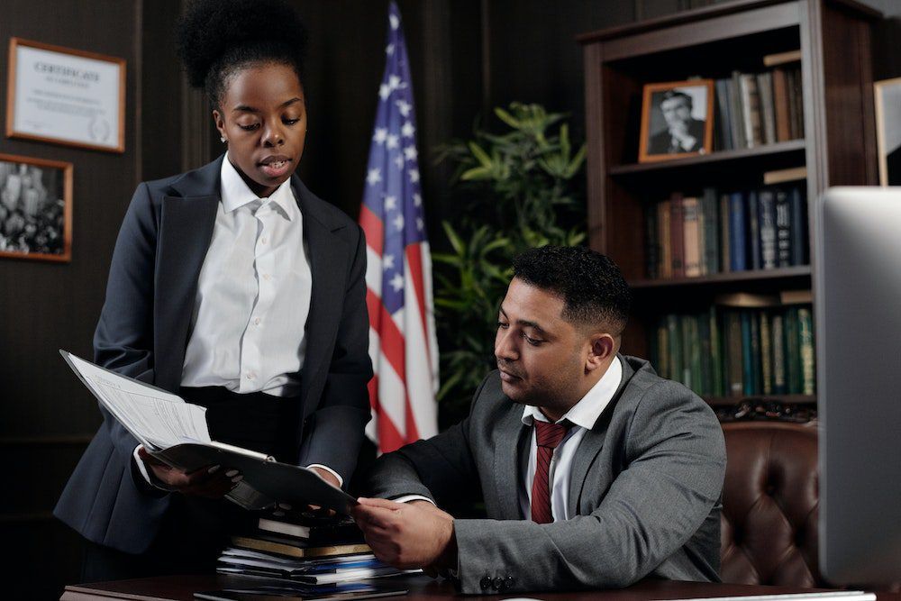 a man and a woman are sitting at a desk in front of an american flag .
