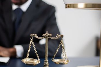 a man in a suit and tie is sitting at a table with a scale of justice in front of him .