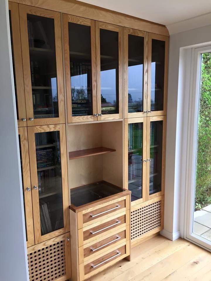 A wooden cabinet with glass doors and drawers in a room next to a window.