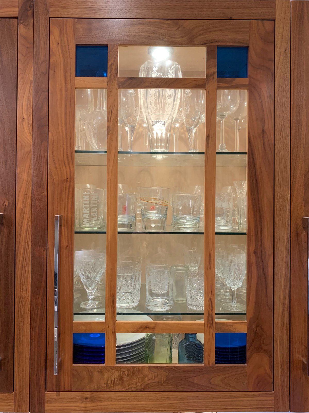 A wooden cabinet with glass shelves filled with glasses and plates.