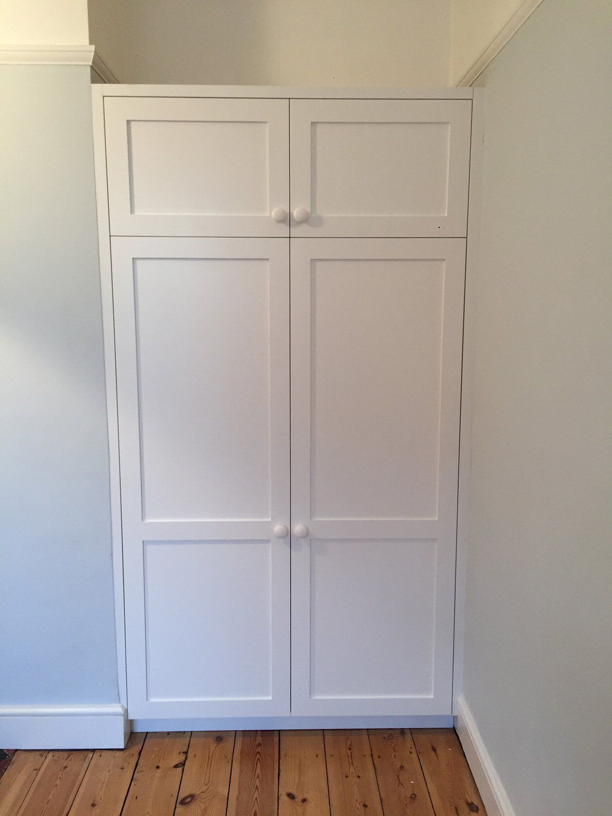 A white wardrobe with two doors and a wooden floor in a room.