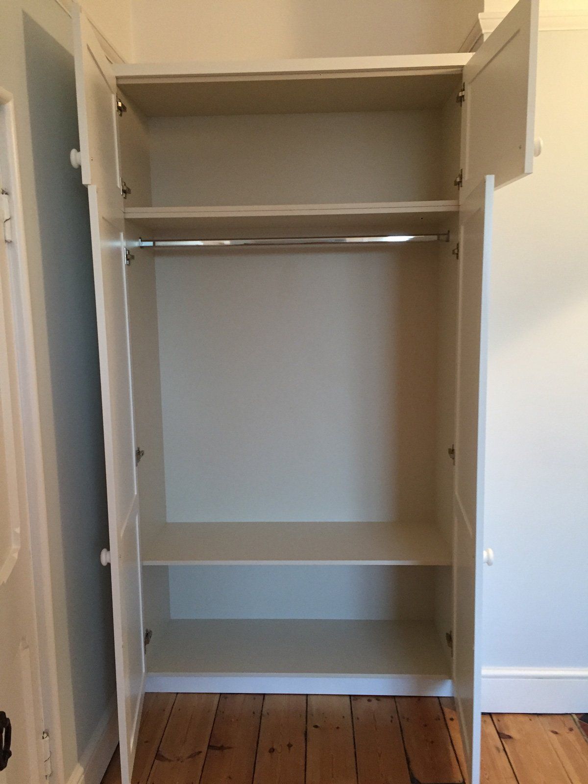 An empty white wardrobe with the doors open and shelves.