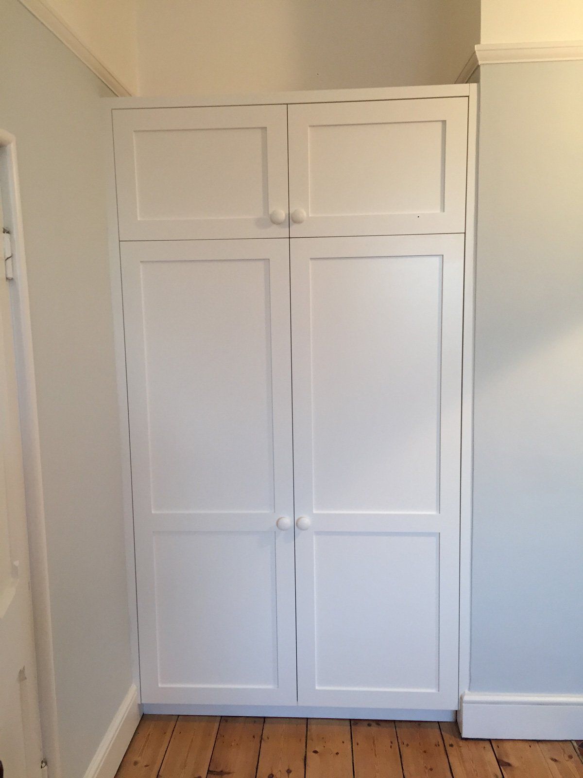 A white cabinet with two doors is in a room with wooden floors.
