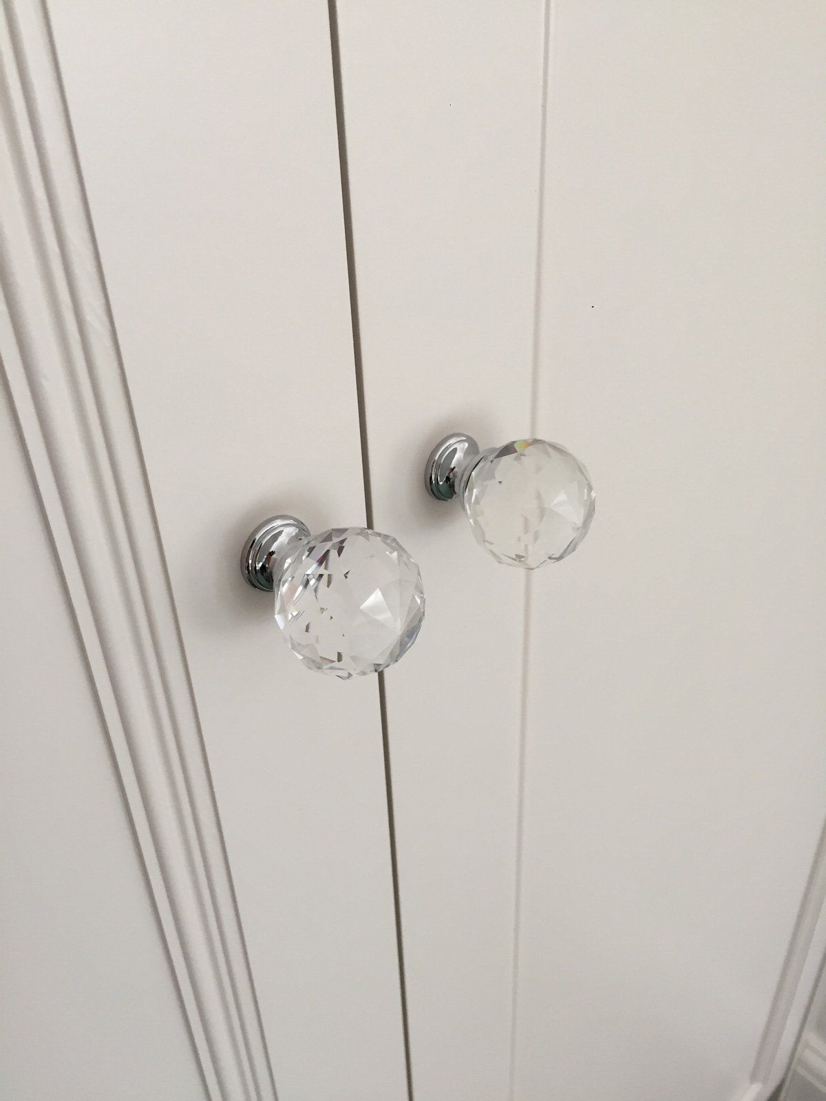 A pair of clear glass door knobs on a white cabinet.