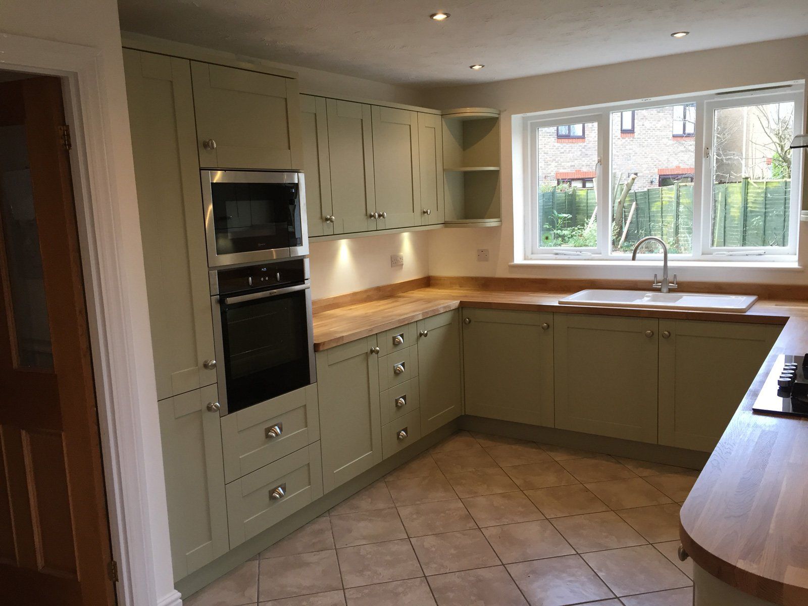 A kitchen with green cabinets , stainless steel appliances , a sink , and a window.
