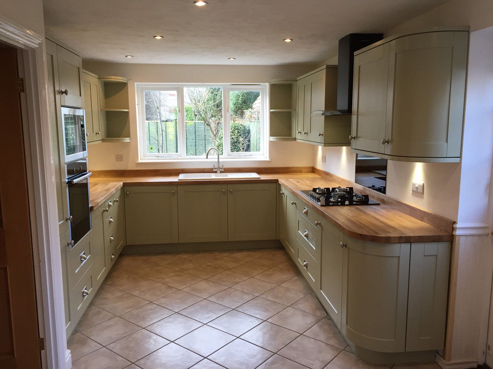 A kitchen with green cabinets and wooden counter tops.