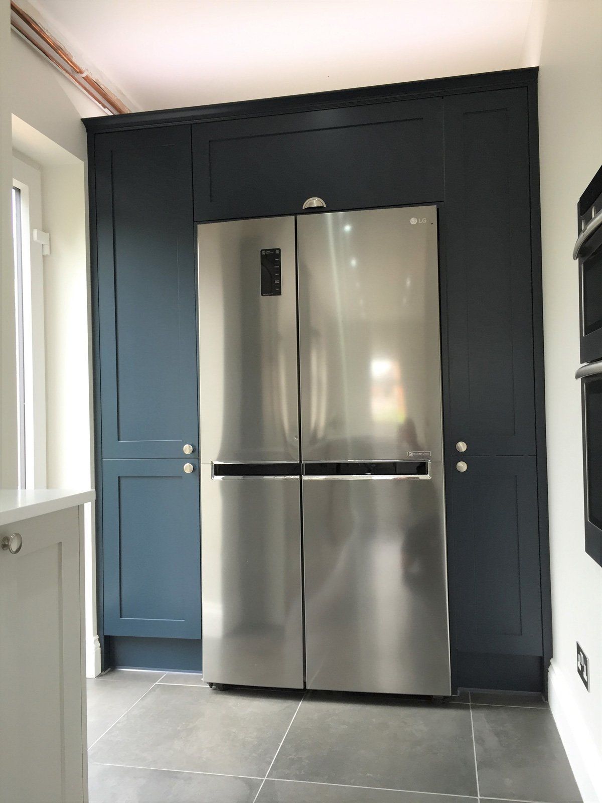 A stainless steel refrigerator in a kitchen with blue cabinets