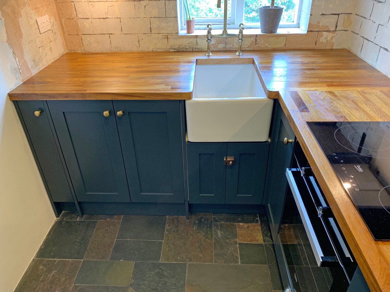 A kitchen with a sink , stove , and wooden counter tops.
