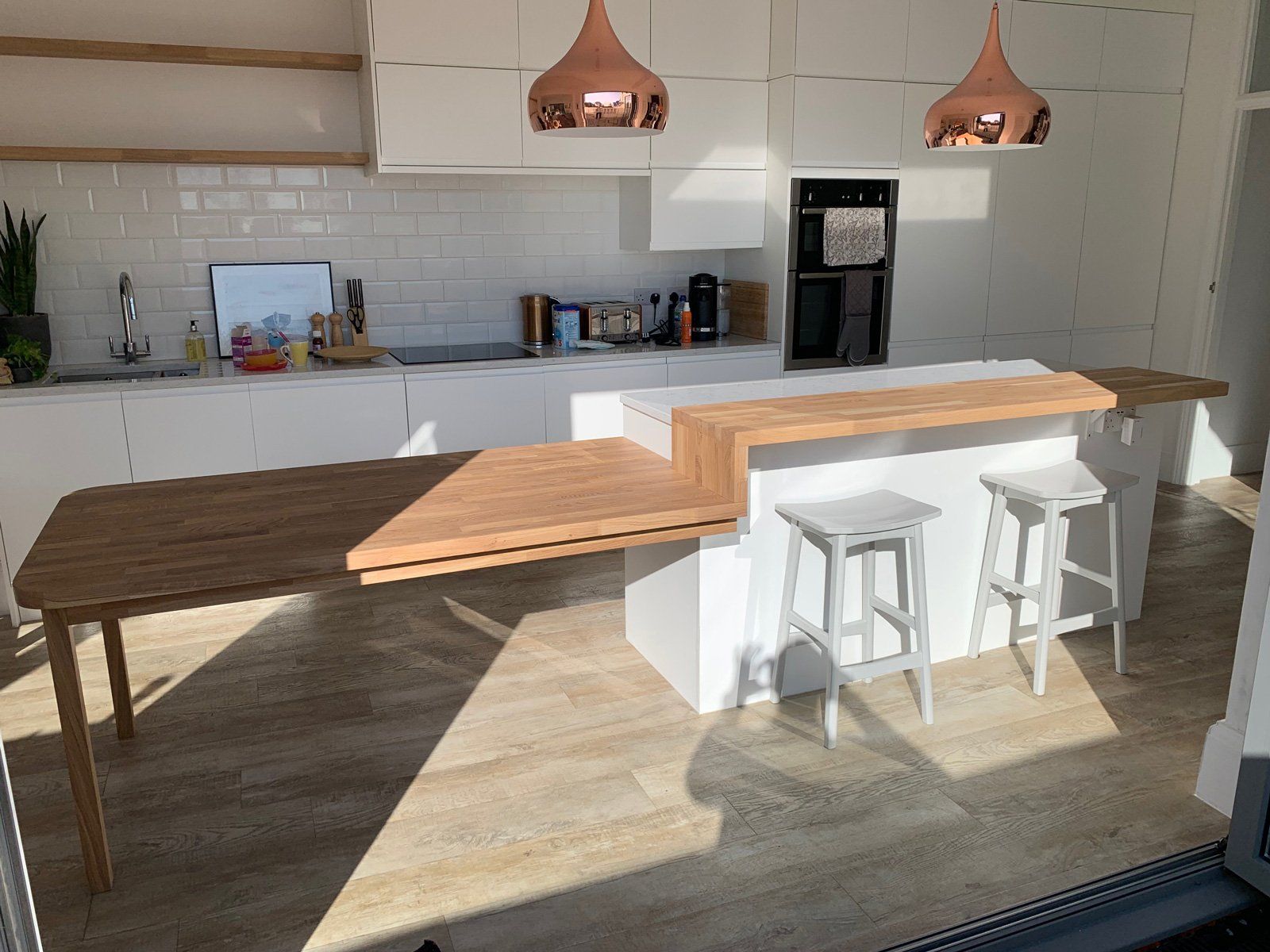A kitchen with white cabinets , a wooden table and stools.