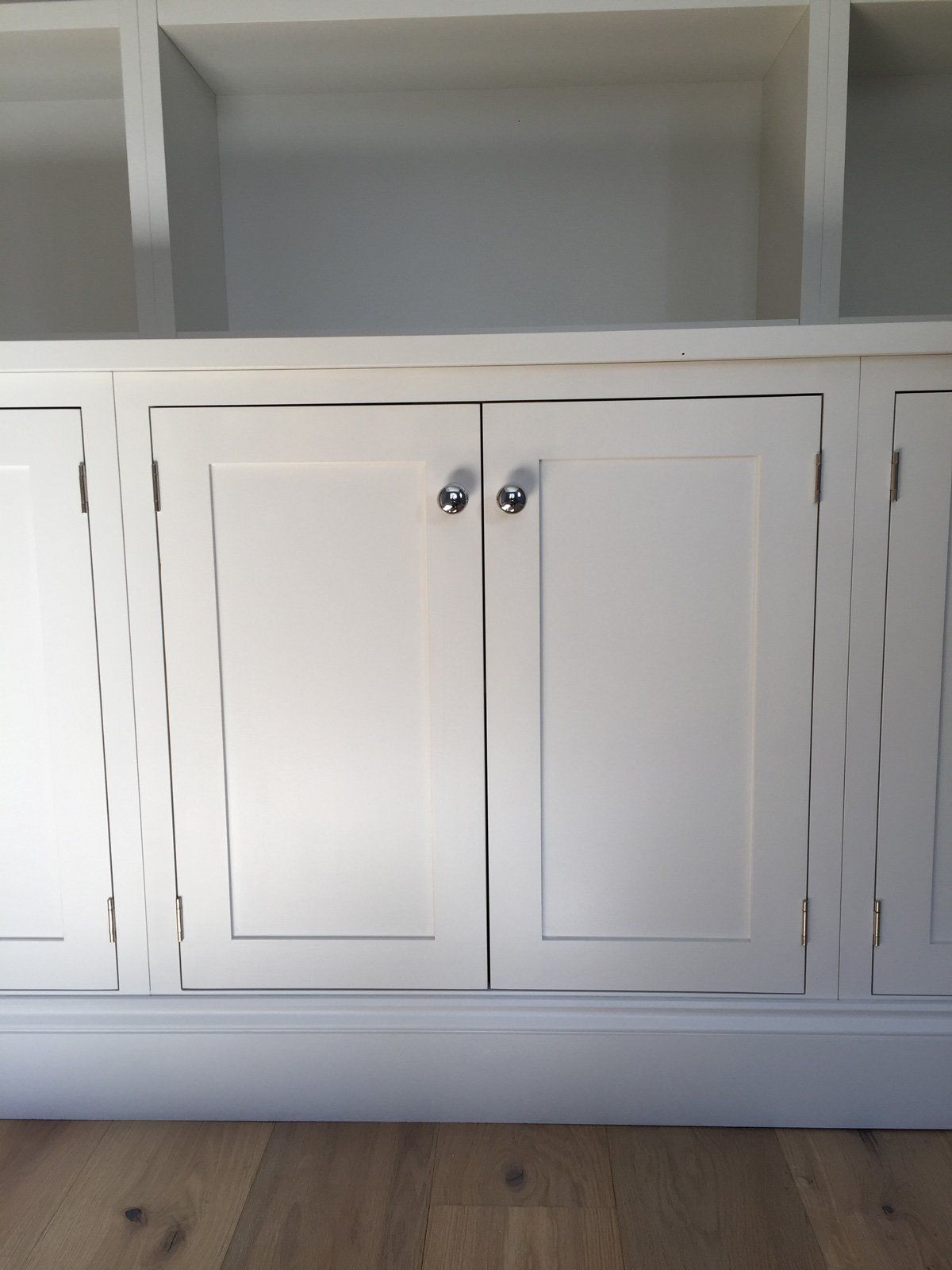 A white cabinet with two doors is sitting on a wooden floor.