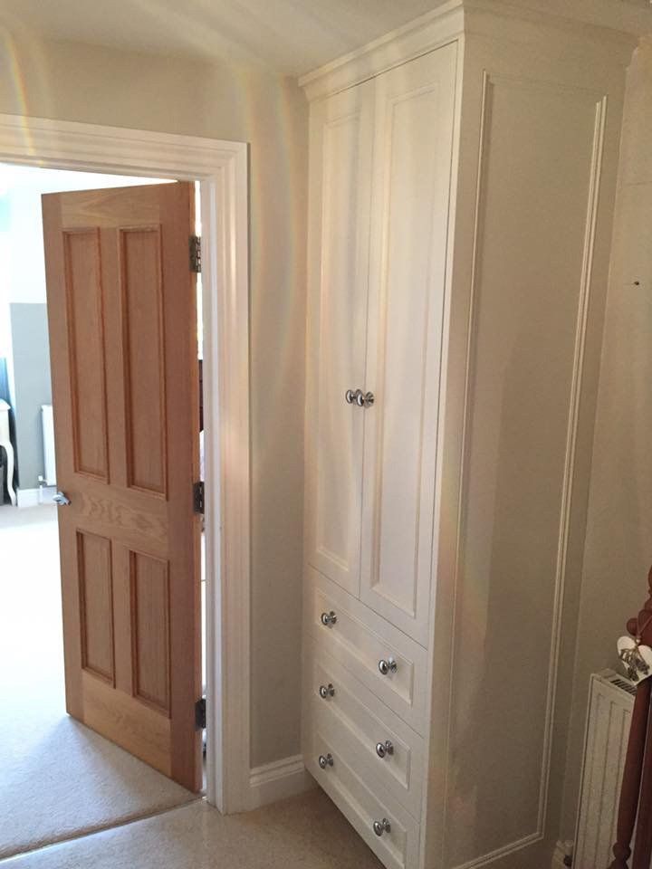 A white cabinet with drawers and a wooden door in a room.